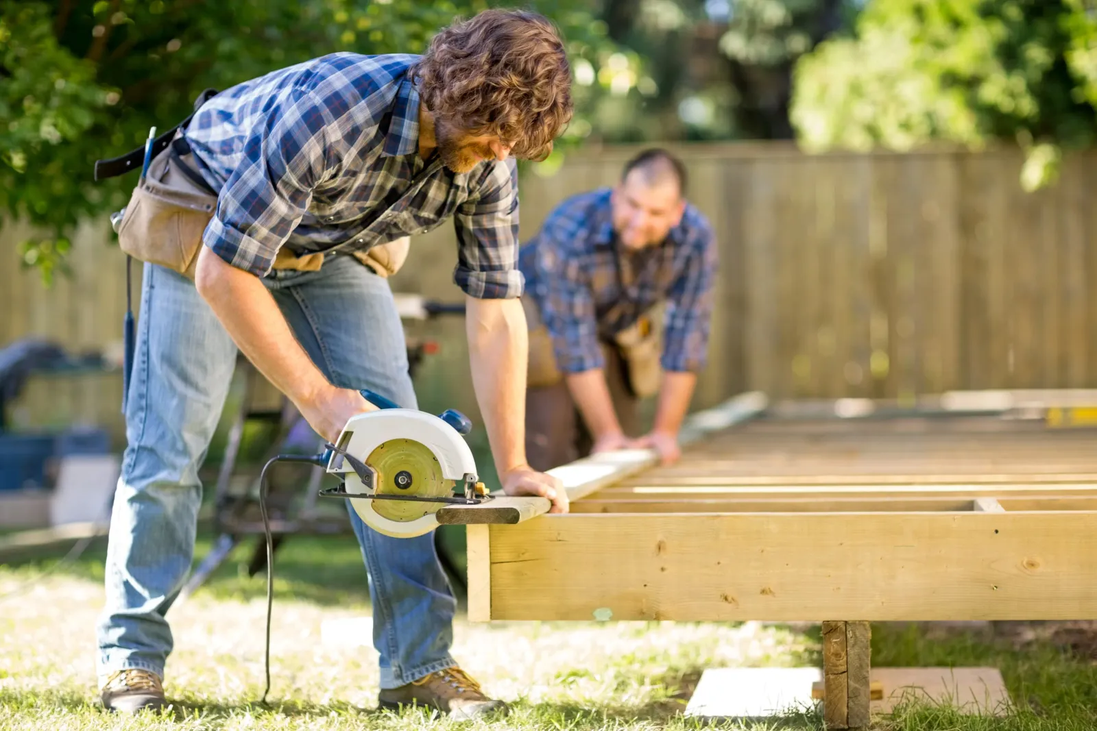 Two contractors work together to cut a wooden board on a job site.
