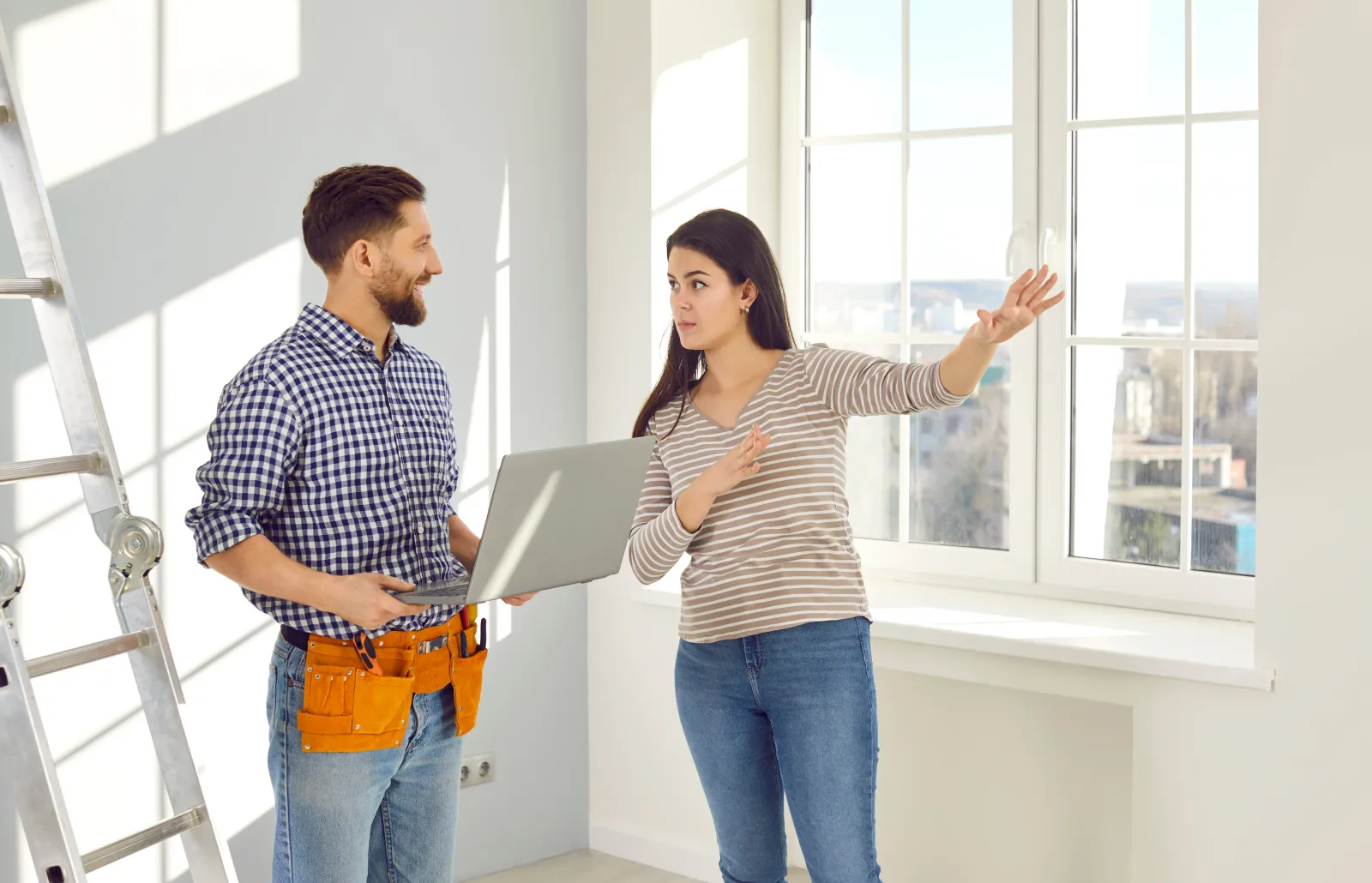 Young woman talking to a repairman who is going to make repairs in her house. Workman with a tool belt and laptop listening a girl homeowner explaining to him what work she needs to done at home